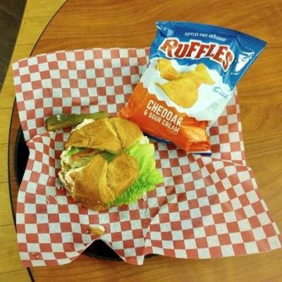 Chicken Salad Sandwich on a croissant with a bag of chips and a pickle.  