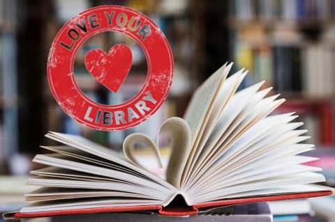 Open book with a heart shaped folded into it and a Love Your Library  stamp