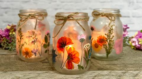 Three jars with pressed flowers on them with a jute string on top against a woodish background. 