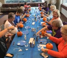 Adults painting pumpkins during library craft day